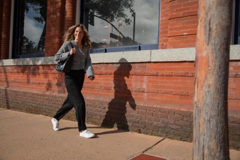 A woman smiling and walking down the street in her White Dillon Leather shoes