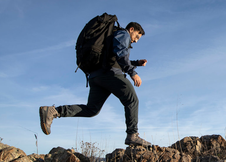 A man wearing Scrambler Mid II boots leaping from one rock to another outside on a hike