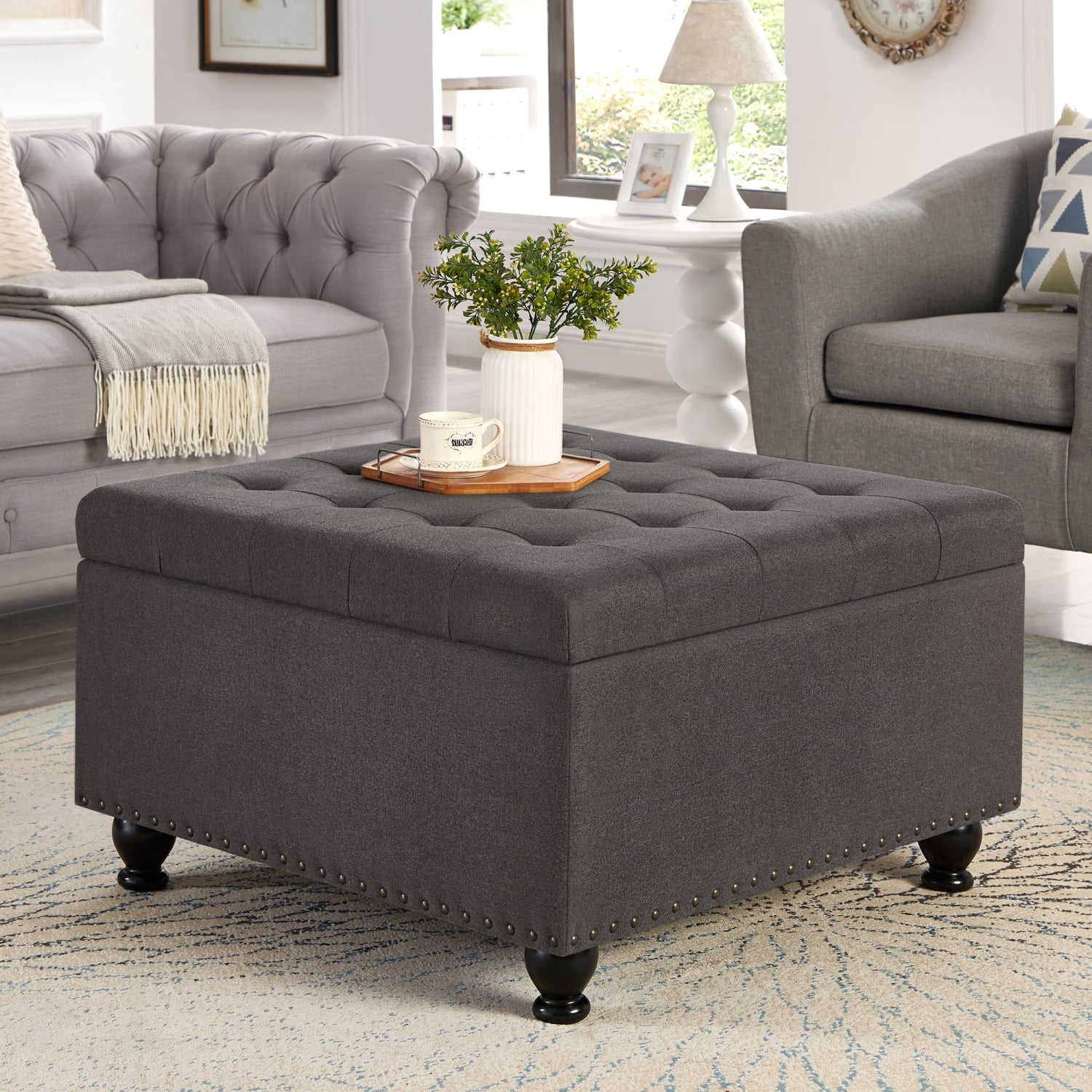 Elegant large dark grey upholstered storage ottoman with stylish nail trims and wooden legs  perfect as a modern button tufted coffee table for your living space.