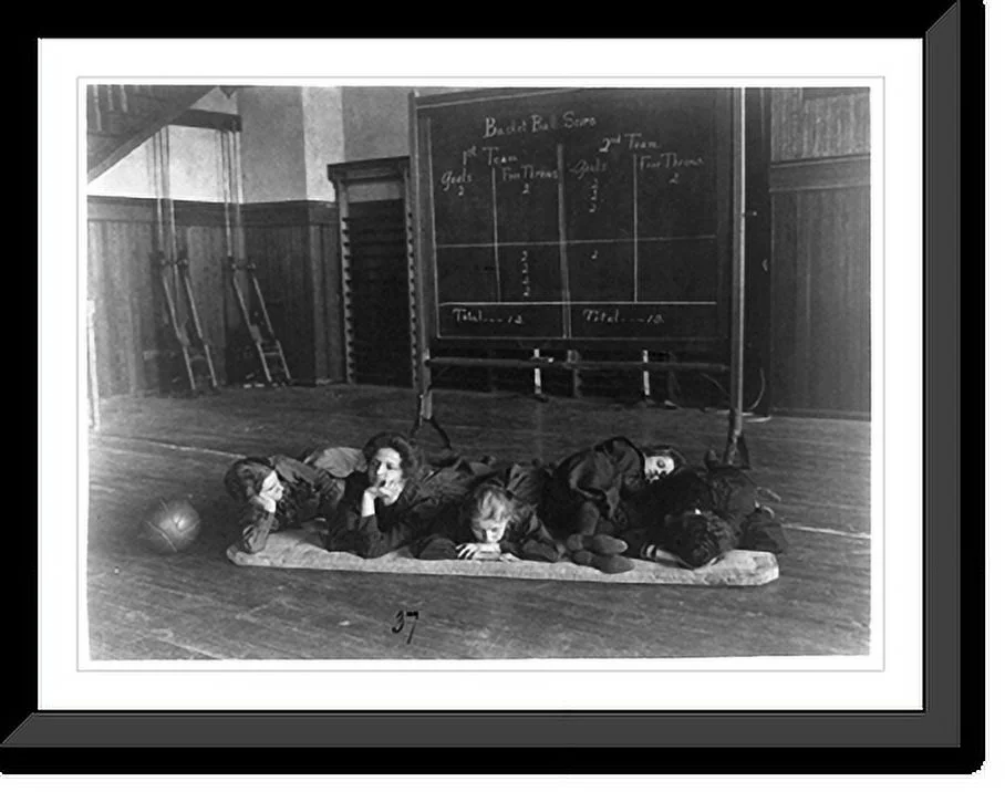 Historic Framed Print, [Five girls lying on mat in gymnasium in front of basketball scoreboard, Western High School, Washington, D.C.], 17-7/8